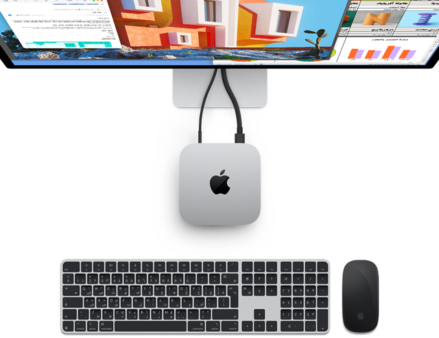 صورة علوية لجهاز Mac mini بلون فضي يحمل شعار Apple، ويظهر موصولاً بشاشة وبجانبه لوحة مفاتيح ماجيك لاسلكية وماجيك ماوس