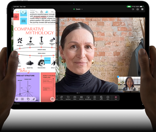 iPad Pro, front exterior, landscape orientation, space black color, rounded corners, black display bezel, hands holding left and right sides, display showing a FaceTime conversation being live translated, and an educational app showing a presentation of "Comparative Mythology" with text, diagrams, and handwritten notes